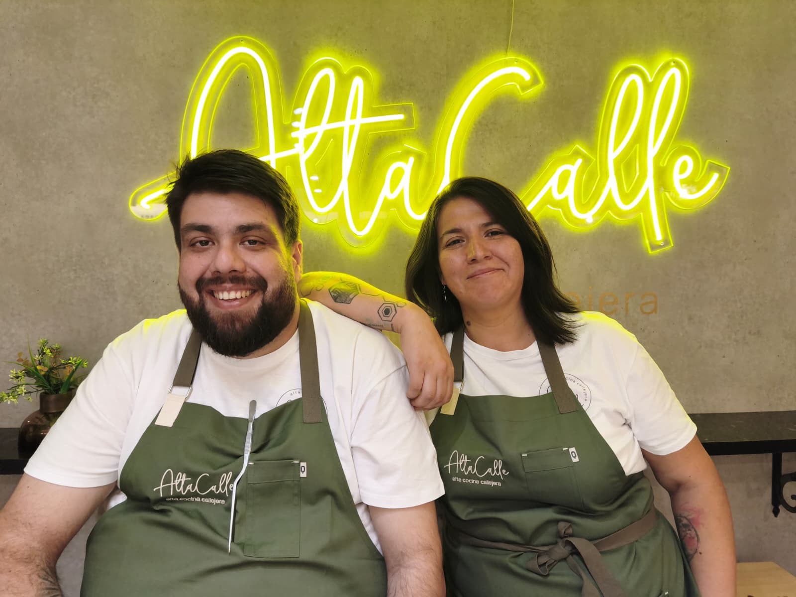 Los socios de AltaCalle sonriendo frente al letrero de neón del local